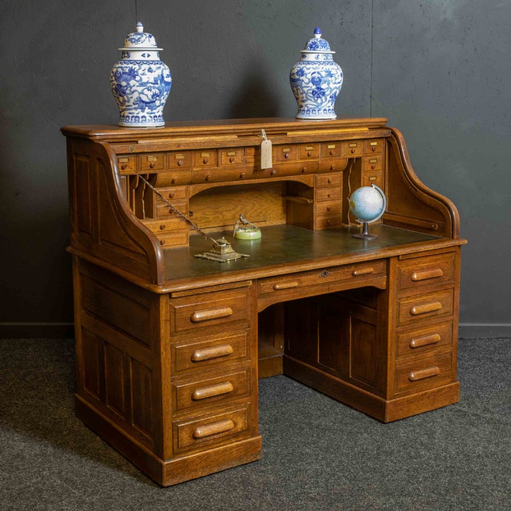 An Edwardian oak roll top desk with a raised slatted tambour front revealing fitted interior compartments above twin pedestal drawers. View III