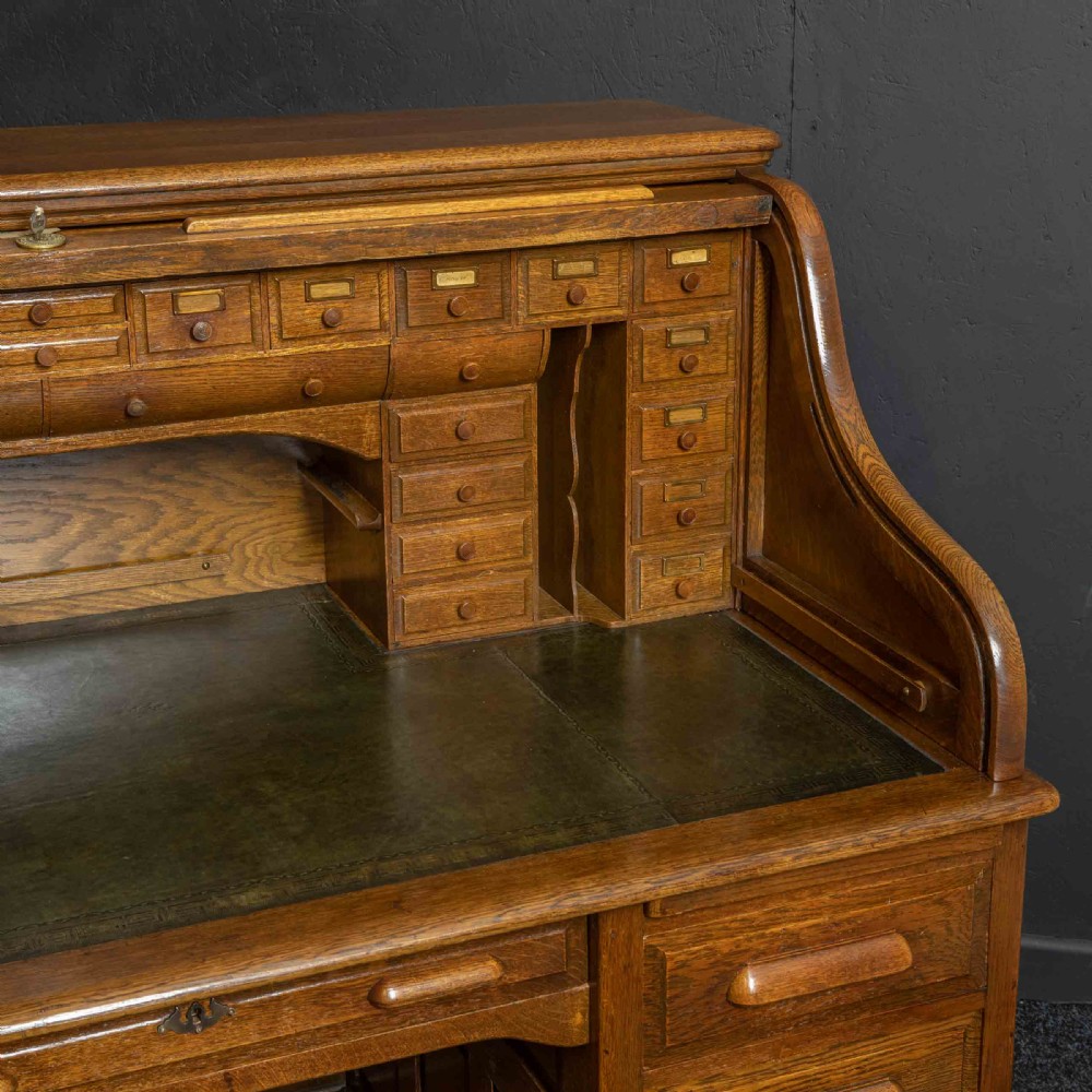 An Edwardian oak roll top desk with a raised slatted tambour front revealing fitted interior compartments above twin pedestal drawers. View V