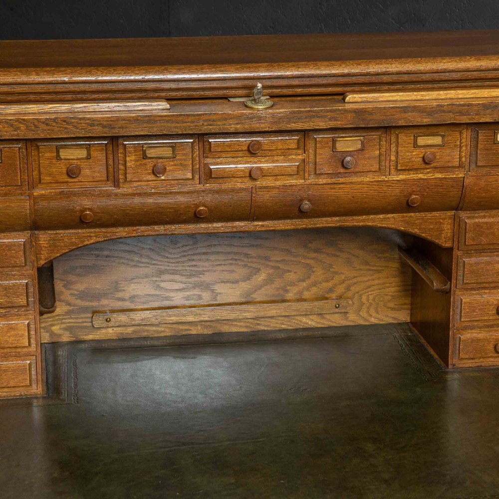 An Edwardian oak roll top desk with a raised slatted tambour front revealing fitted interior compartments above twin pedestal drawers. View VI