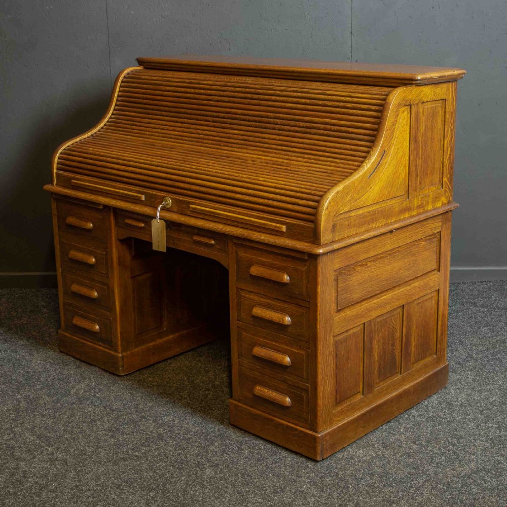 An Edwardian oak roll top desk with a raised slatted tambour front revealing fitted interior compartments above twin pedestal drawers. View XII