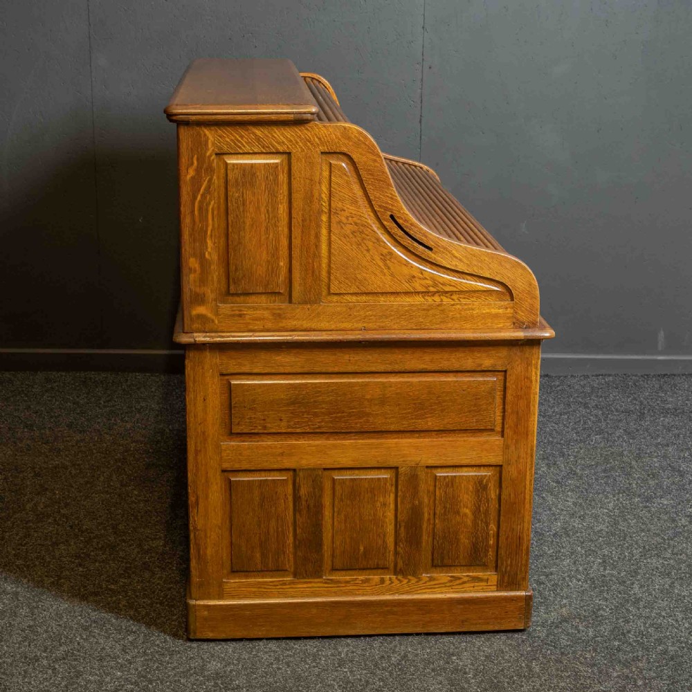 An Edwardian oak roll top desk with a raised slatted tambour front revealing fitted interior compartments above twin pedestal drawers. View XVII