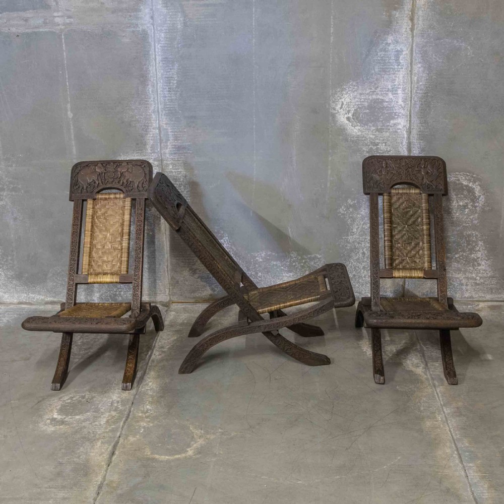 A set of three dark hand-carved wooden folding chairs featuring ornate foliate reliefs and woven rattan seat panels. View II