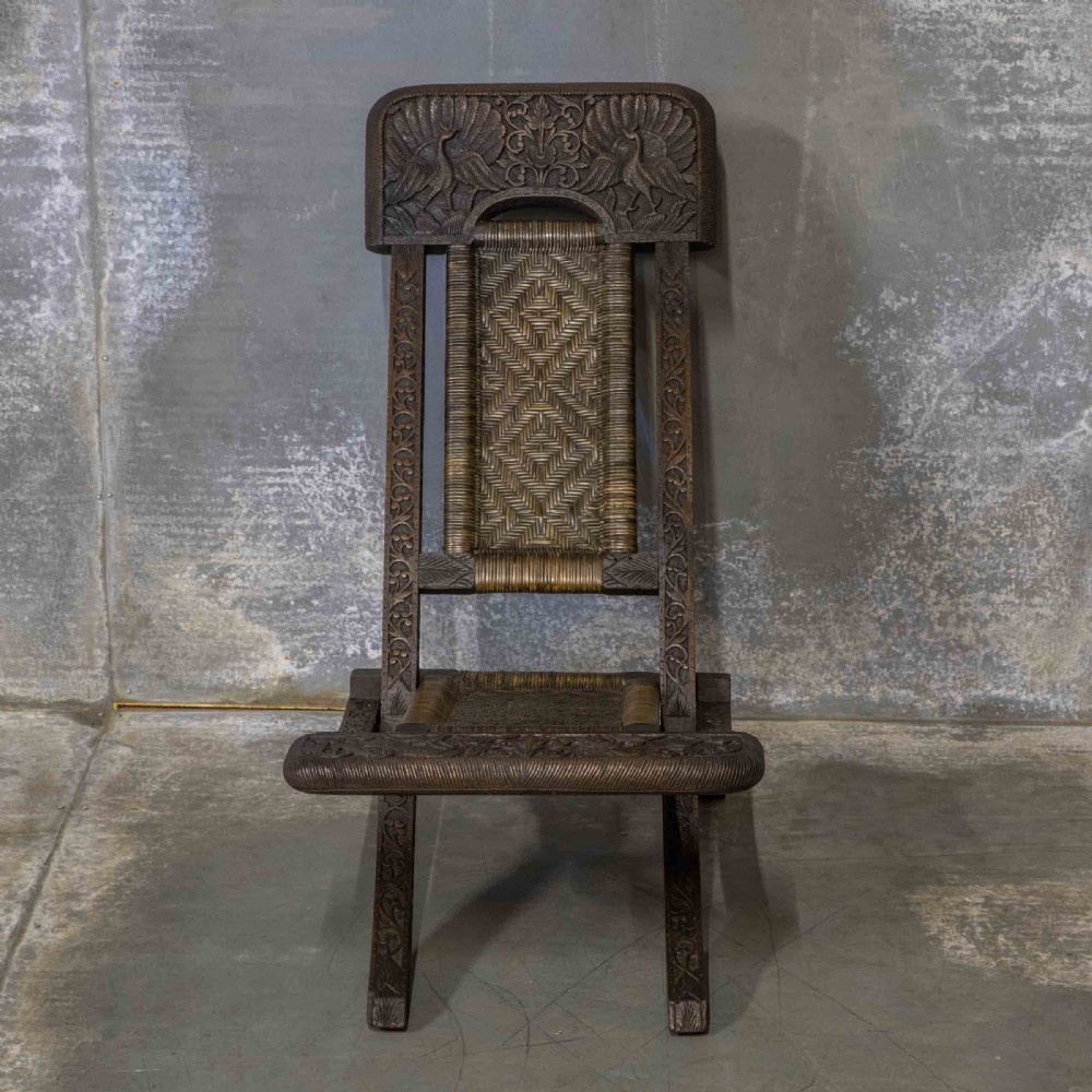 A set of three dark hand-carved wooden folding chairs featuring ornate foliate reliefs and woven rattan seat panels. View IV