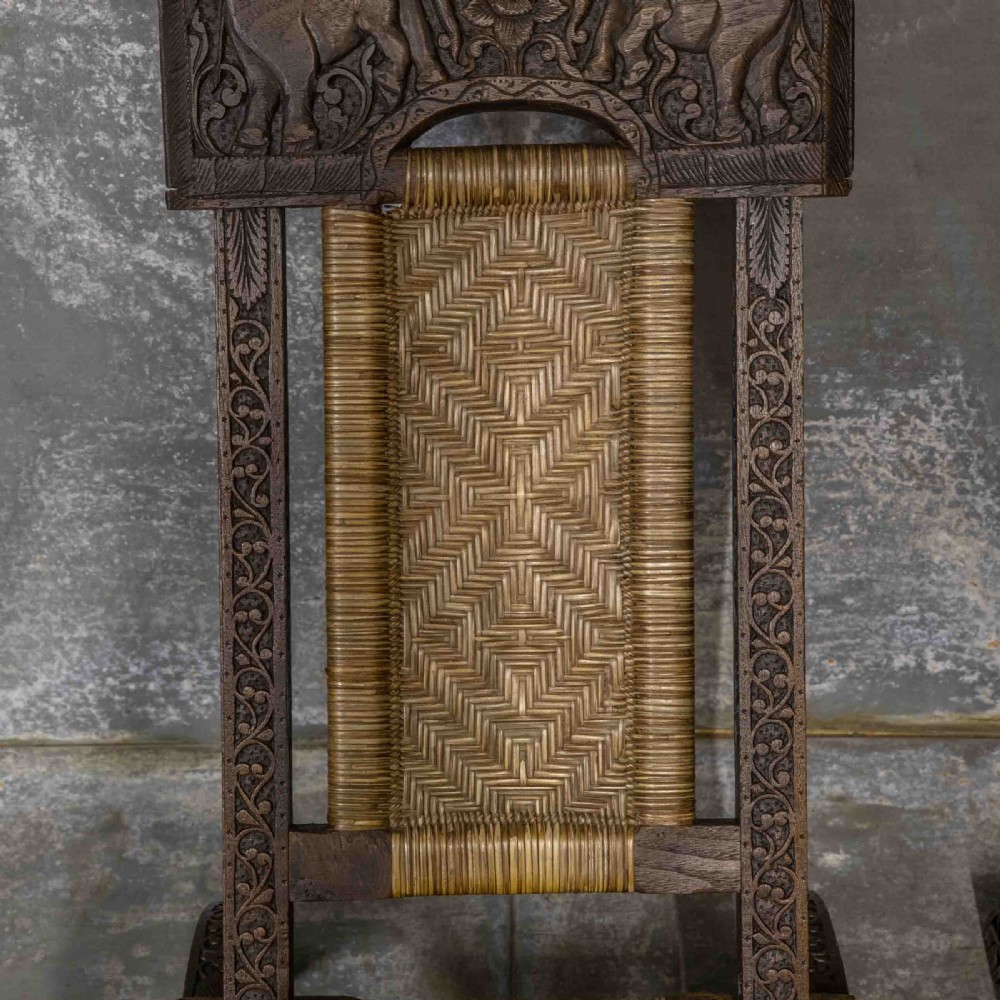 A set of three dark hand-carved wooden folding chairs featuring ornate foliate reliefs and woven rattan seat panels. View V