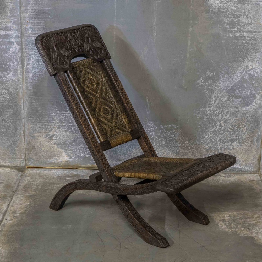 A set of three dark hand-carved wooden folding chairs featuring ornate foliate reliefs and woven rattan seat panels. View VII