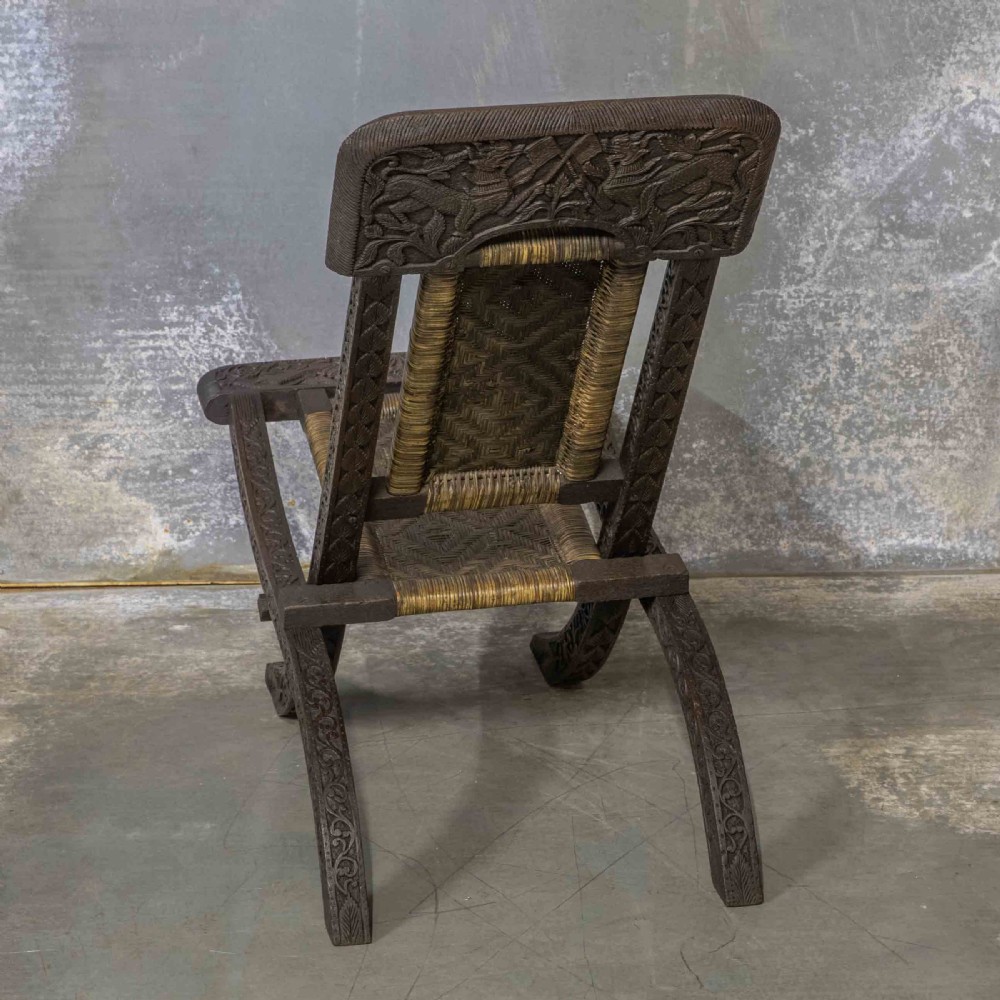 A set of three dark hand-carved wooden folding chairs featuring ornate foliate reliefs and woven rattan seat panels. View IX