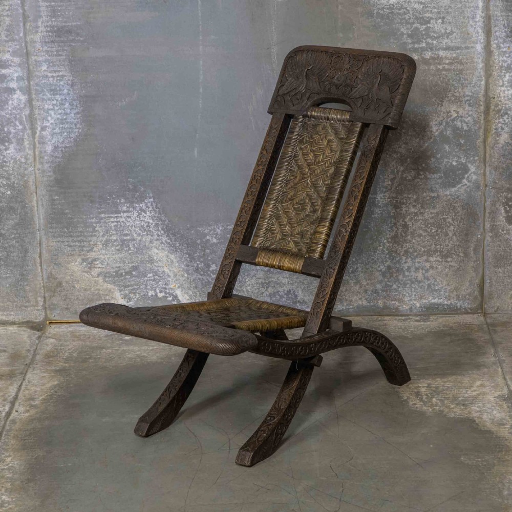 A set of three dark hand-carved wooden folding chairs featuring ornate foliate reliefs and woven rattan seat panels. View XI