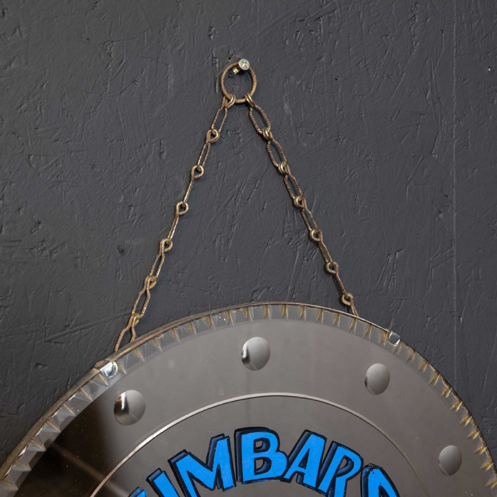 A circular frameless wall mirror featuring blue typography that reads Zimbars Jazz Club, suspended by a top chain. View III