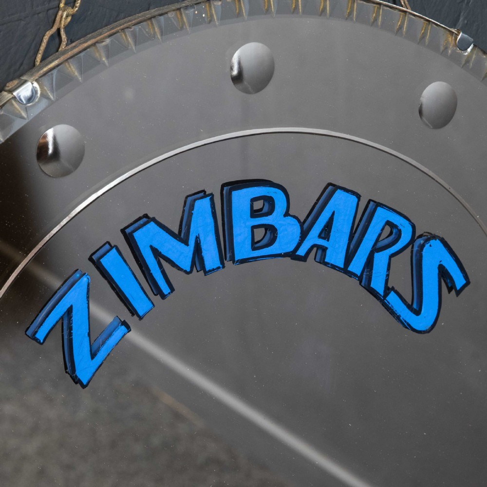 A circular frameless wall mirror featuring blue typography that reads Zimbars Jazz Club, suspended by a top chain. View VI