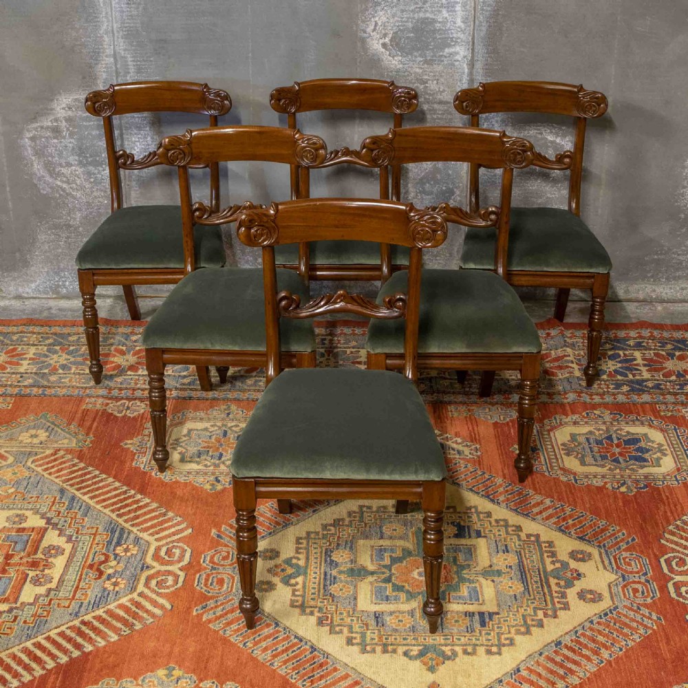 A set of six William IV mahogany dining chairs featuring carved top rails, turned front legs, and green velvet upholstered seats.