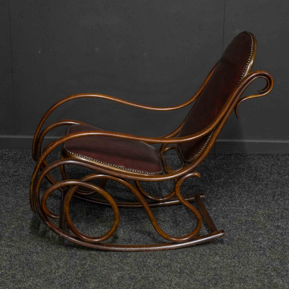 An antique Thonet steam-bent wood rocking chair featuring dark brown leather upholstered seating and brass studding along the frame.