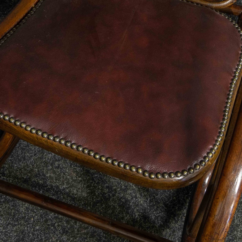 An antique Thonet steam-bent wood rocking chair featuring dark brown leather upholstered seating and brass studding along the frame. View IV