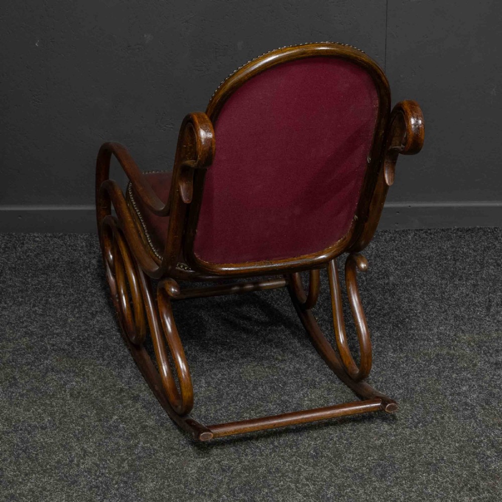 An antique Thonet steam-bent wood rocking chair featuring dark brown leather upholstered seating and brass studding along the frame. View VII
