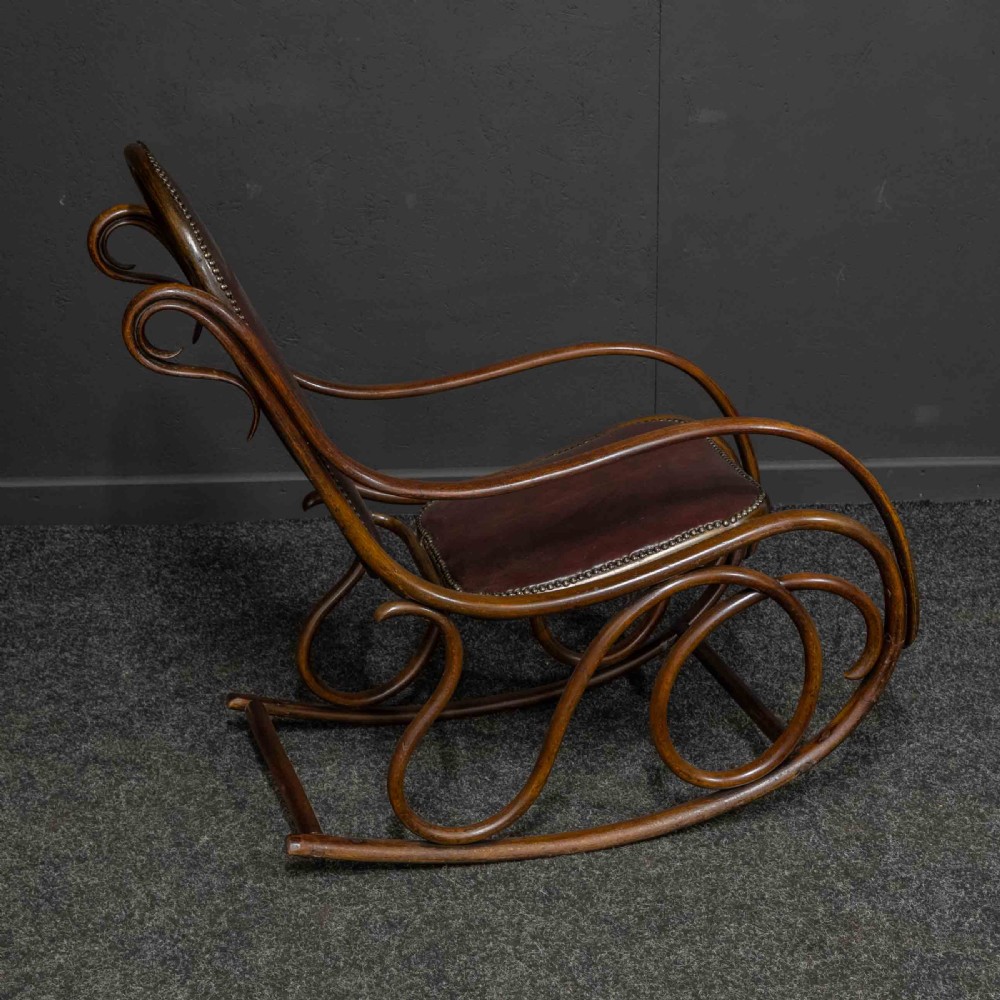 An antique Thonet steam-bent wood rocking chair featuring dark brown leather upholstered seating and brass studding along the frame. View VIII