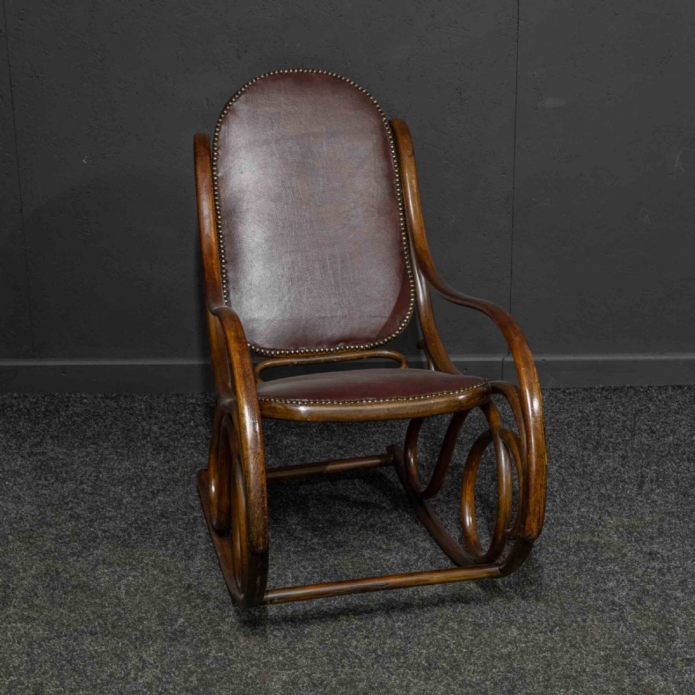 An antique Thonet steam-bent wood rocking chair featuring dark brown leather upholstered seating and brass studding along the frame. View IX