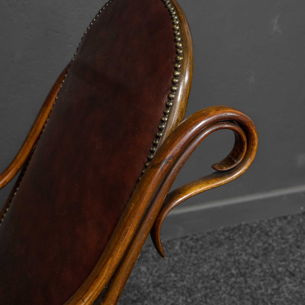 An antique Thonet steam-bent wood rocking chair featuring dark brown leather upholstered seating and brass studding along the frame. View XI
