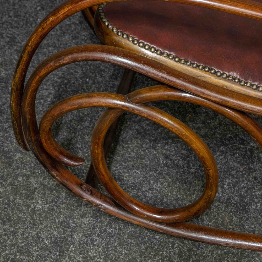 An antique Thonet steam-bent wood rocking chair featuring dark brown leather upholstered seating and brass studding along the frame. View XII