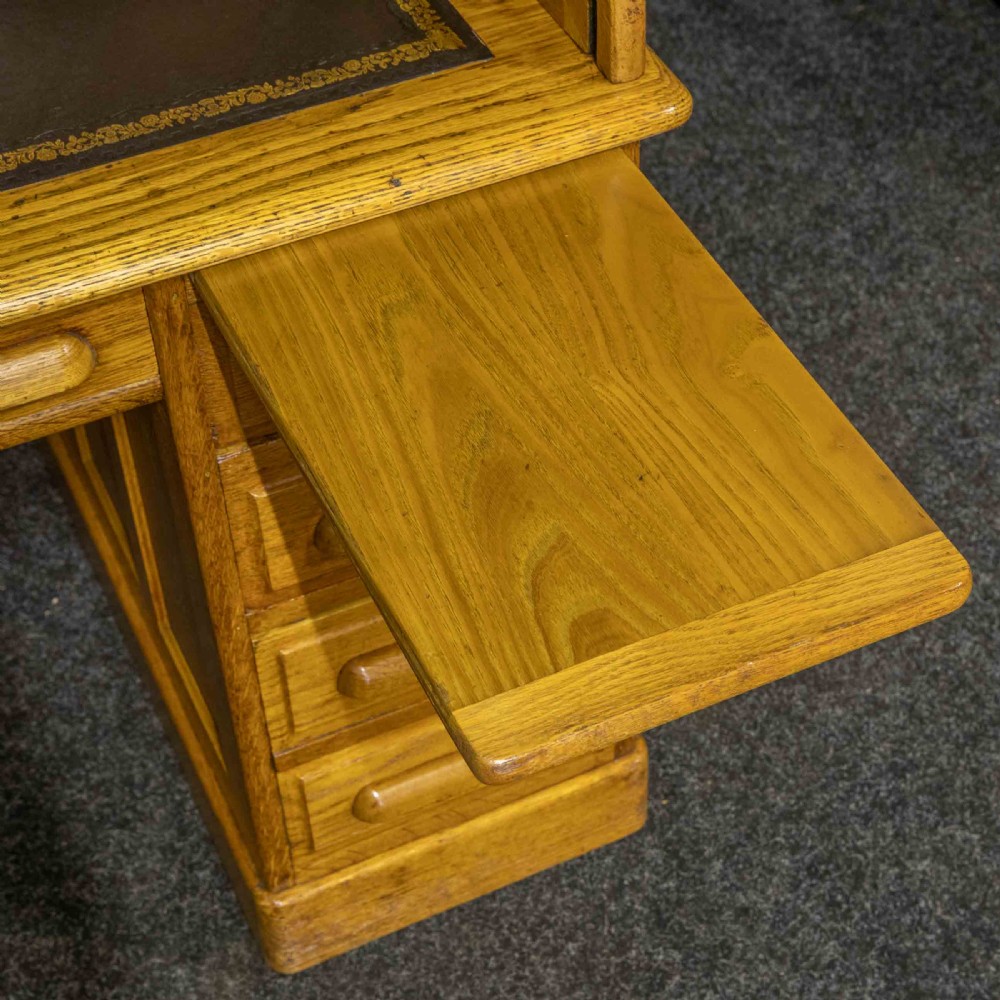 An early 20th-century golden oak roll top desk featuring open fitted pigeonhole compartments, a dark leather writing inset, and twin drawer pedestals. View VIII