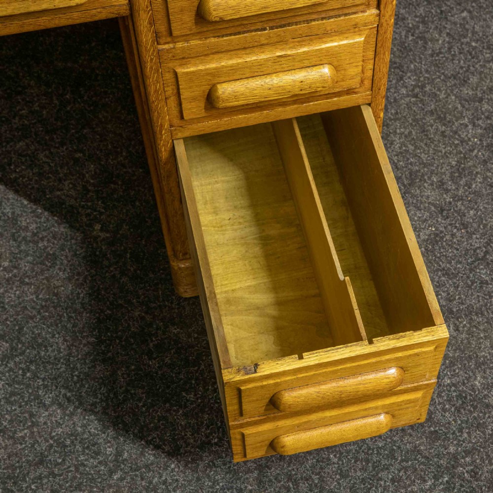 An early 20th-century golden oak roll top desk featuring open fitted pigeonhole compartments, a dark leather writing inset, and twin drawer pedestals. View XI
