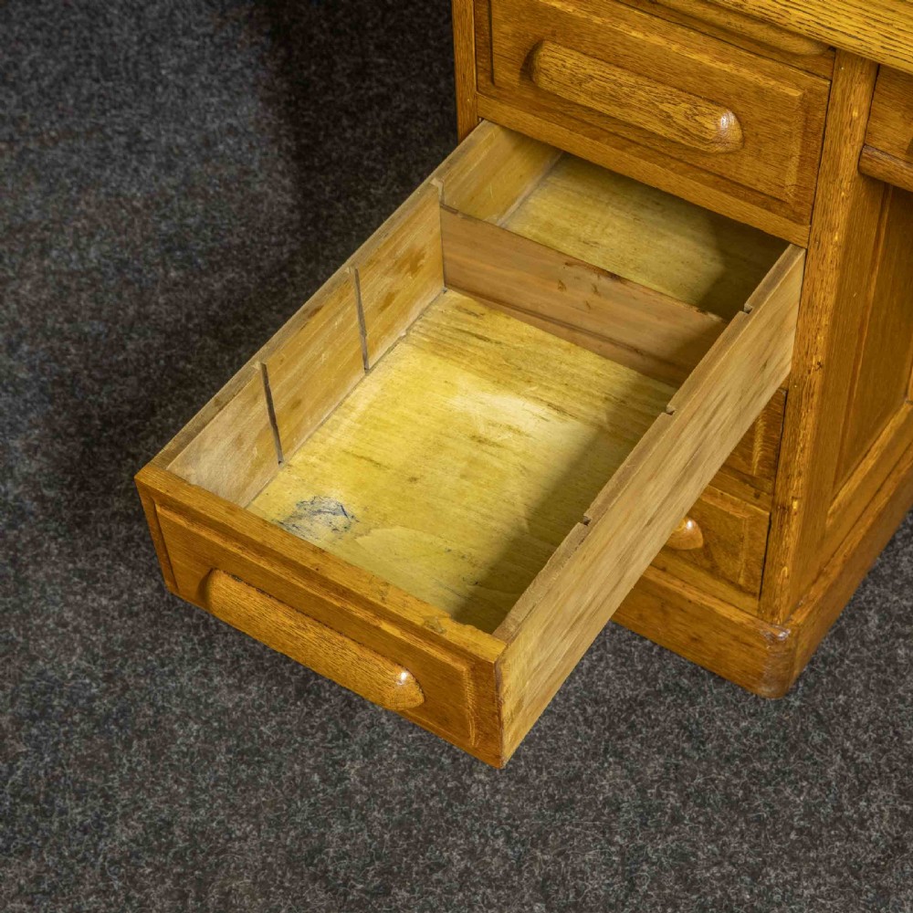 An early 20th-century golden oak roll top desk featuring open fitted pigeonhole compartments, a dark leather writing inset, and twin drawer pedestals. View XII
