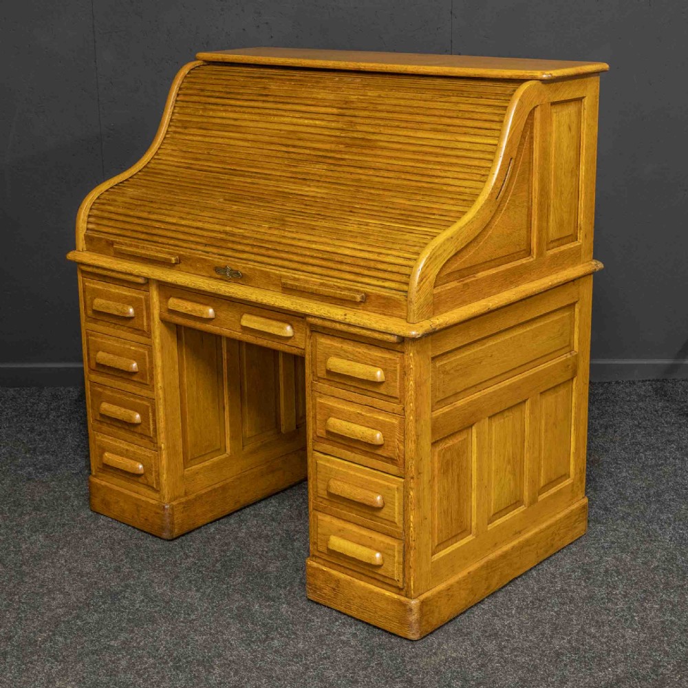 An early 20th-century golden oak roll top desk featuring open fitted pigeonhole compartments, a dark leather writing inset, and twin drawer pedestals. View XIII