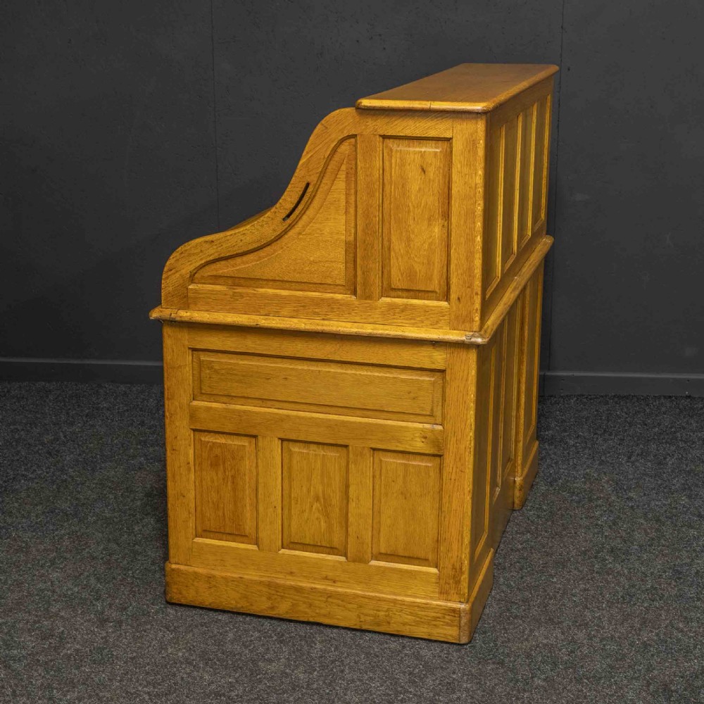 An early 20th-century golden oak roll top desk featuring open fitted pigeonhole compartments, a dark leather writing inset, and twin drawer pedestals. View XIV