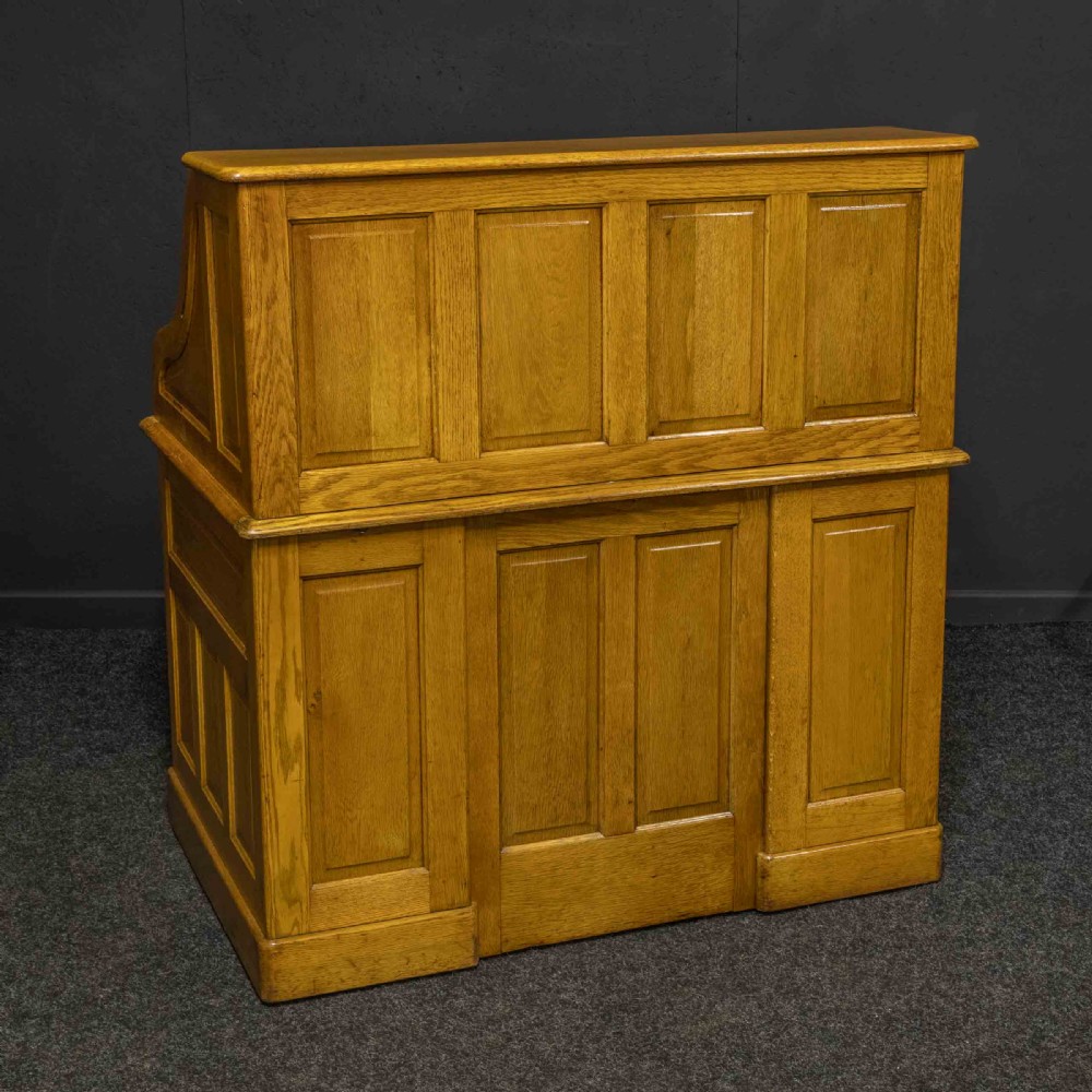 An early 20th-century golden oak roll top desk featuring open fitted pigeonhole compartments, a dark leather writing inset, and twin drawer pedestals. View XV