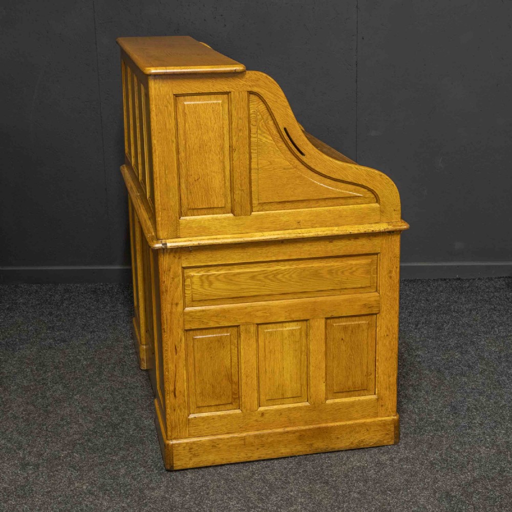 An early 20th-century golden oak roll top desk featuring open fitted pigeonhole compartments, a dark leather writing inset, and twin drawer pedestals. View XVI