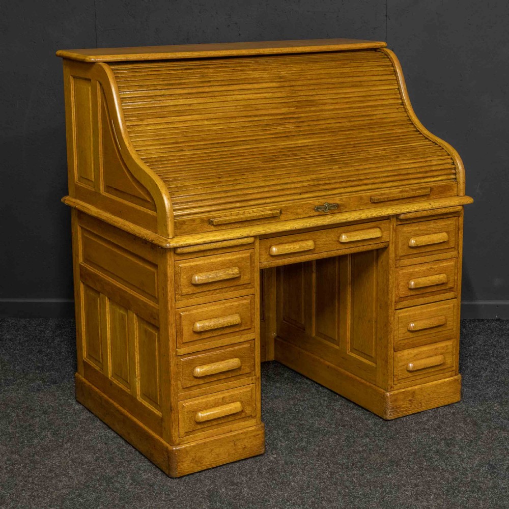An early 20th-century golden oak roll top desk featuring open fitted pigeonhole compartments, a dark leather writing inset, and twin drawer pedestals. View XVII