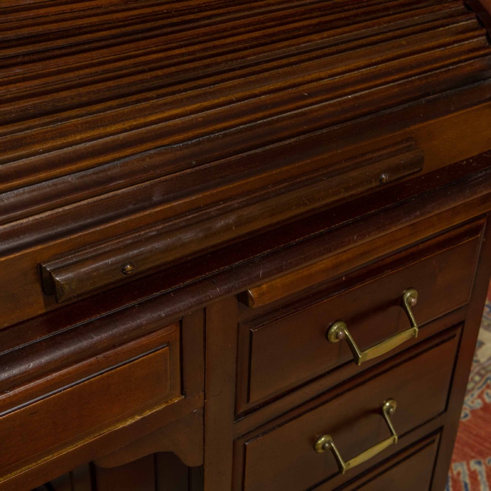 A mahogany roll top desk featuring a curved tambour shutter, internal pigeonhole compartments, a green leather inset writing surface, and twin pedestal drawers with brass drop handles. View IV
