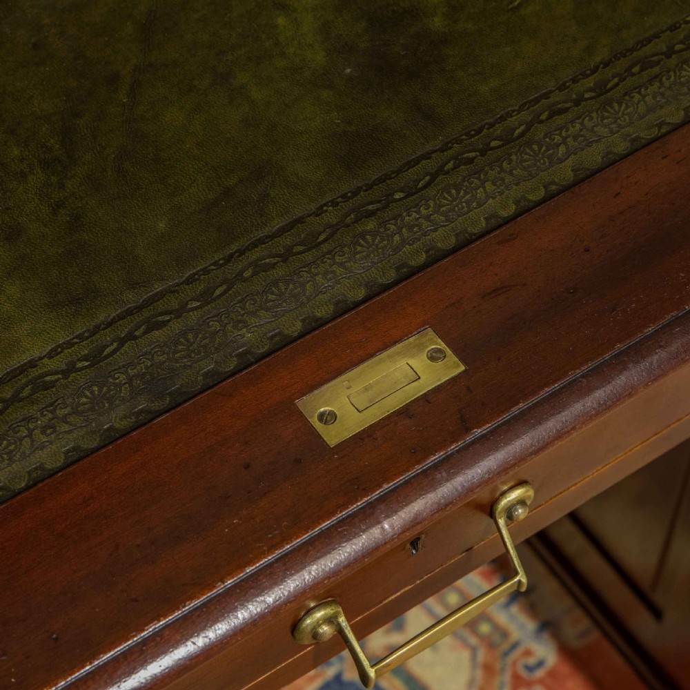 A mahogany roll top desk featuring a curved tambour shutter, internal pigeonhole compartments, a green leather inset writing surface, and twin pedestal drawers with brass drop handles. View VI
