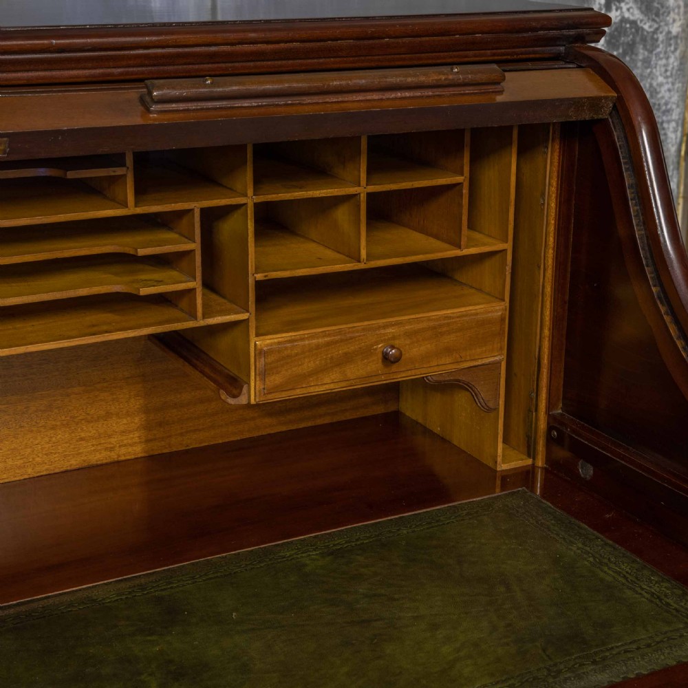 A mahogany roll top desk featuring a curved tambour shutter, internal pigeonhole compartments, a green leather inset writing surface, and twin pedestal drawers with brass drop handles. View VIII