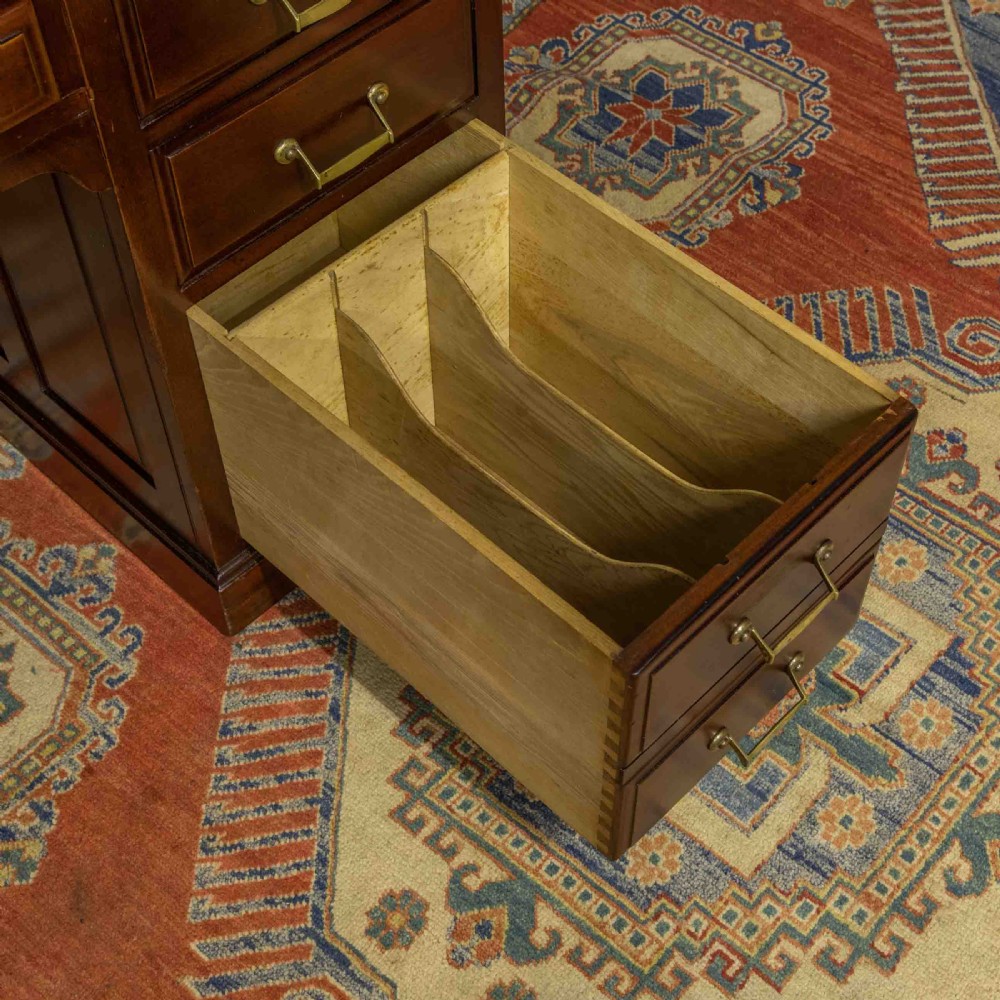 A mahogany roll top desk featuring a curved tambour shutter, internal pigeonhole compartments, a green leather inset writing surface, and twin pedestal drawers with brass drop handles. View X