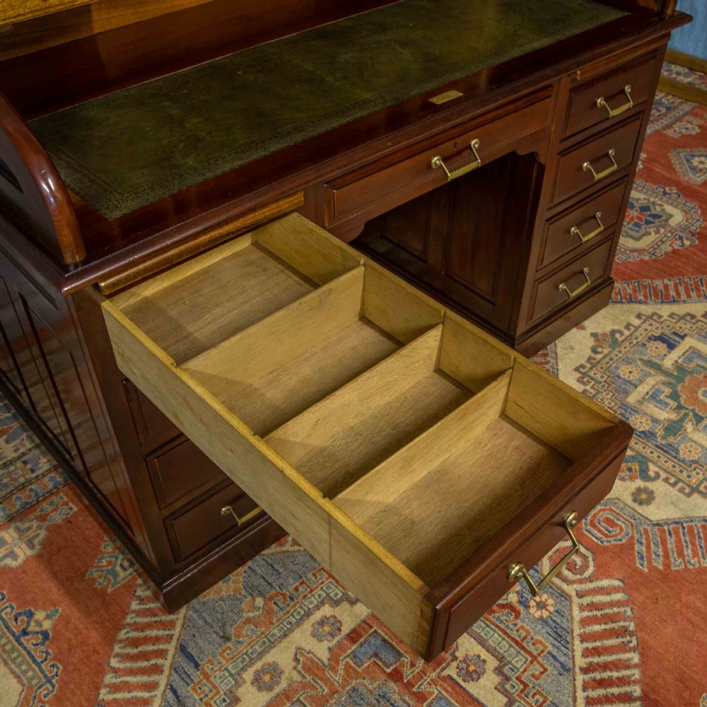 A mahogany roll top desk featuring a curved tambour shutter, internal pigeonhole compartments, a green leather inset writing surface, and twin pedestal drawers with brass drop handles. View XI