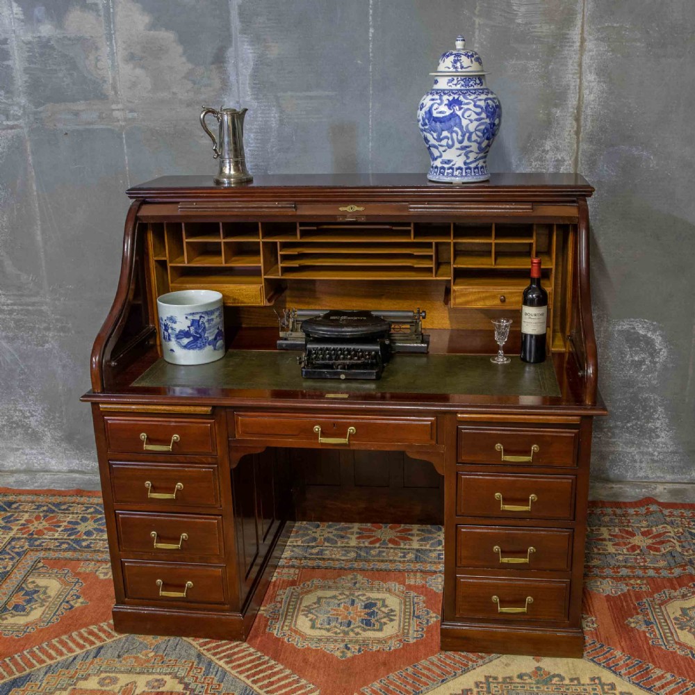 A mahogany roll top desk featuring a curved tambour shutter, internal pigeonhole compartments, a green leather inset writing surface, and twin pedestal drawers with brass drop handles. View XII