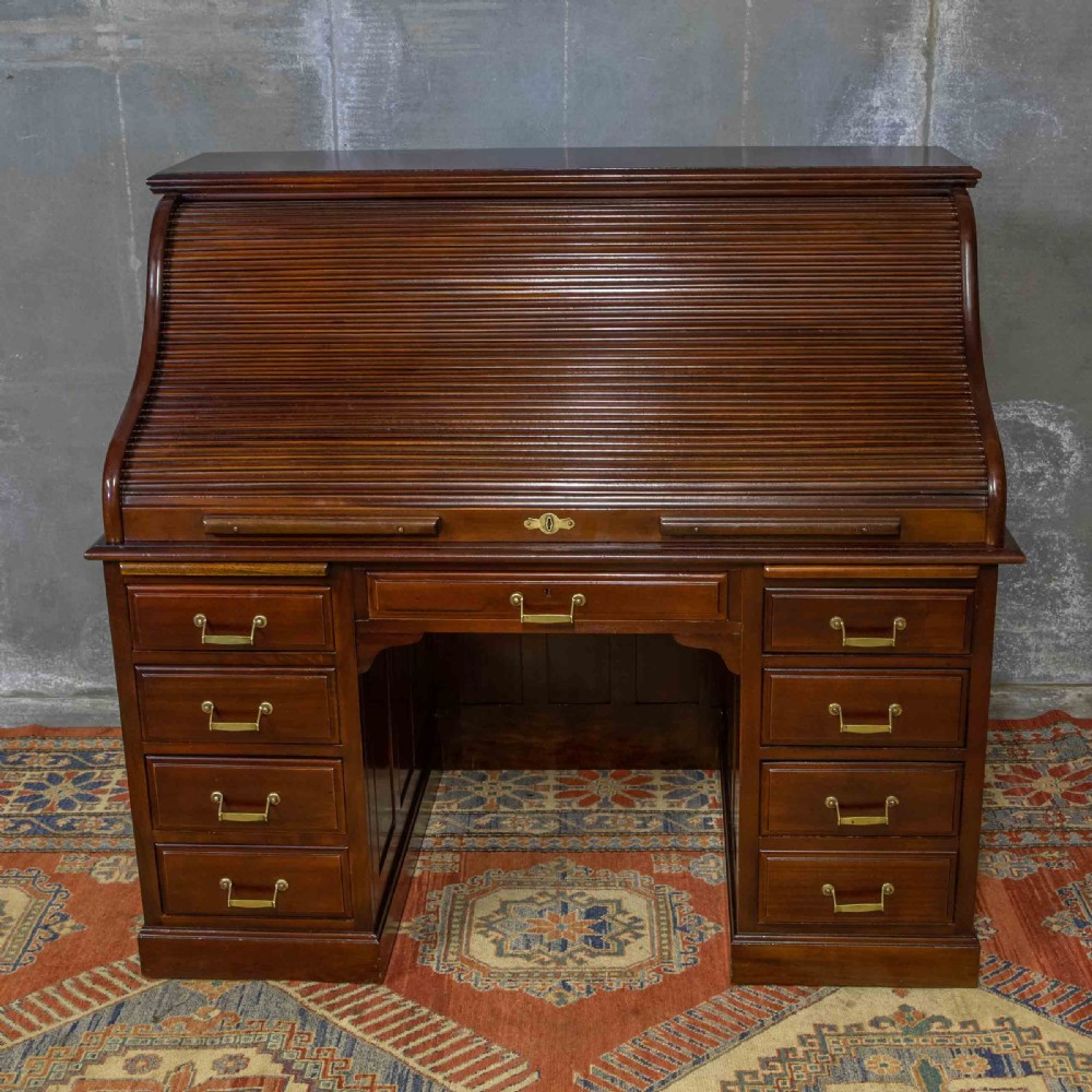 A mahogany roll top desk featuring a curved tambour shutter, internal pigeonhole compartments, a green leather inset writing surface, and twin pedestal drawers with brass drop handles. View XIII