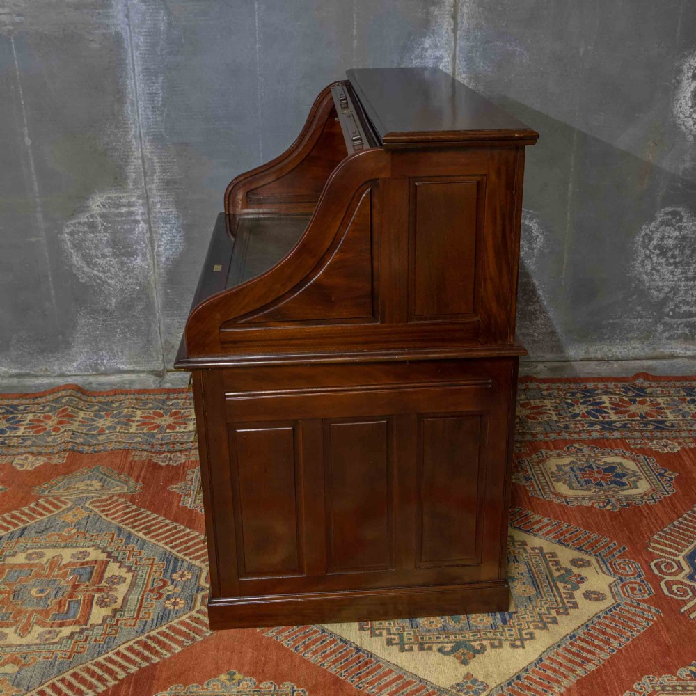 A mahogany roll top desk featuring a curved tambour shutter, internal pigeonhole compartments, a green leather inset writing surface, and twin pedestal drawers with brass drop handles. View XVIII