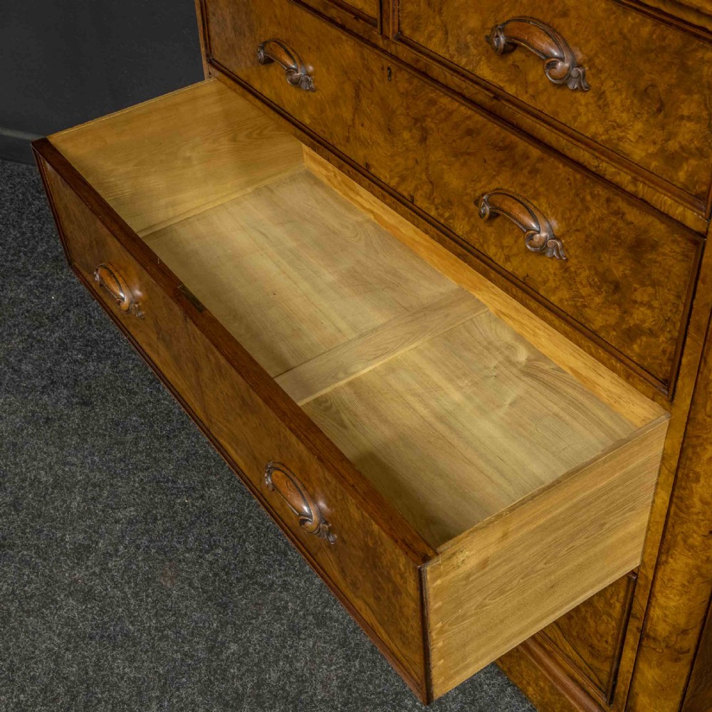 A Victorian burr walnut chest of drawers featuring a two-over-three drawer arrangement with carved handles and rounded corners on a plinth base. View VIII