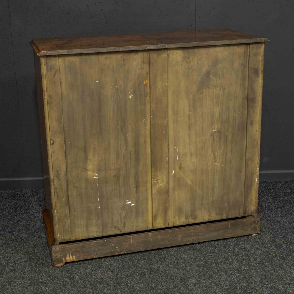A Victorian burr walnut chest of drawers featuring a two-over-three drawer arrangement with carved handles and rounded corners on a plinth base. View X