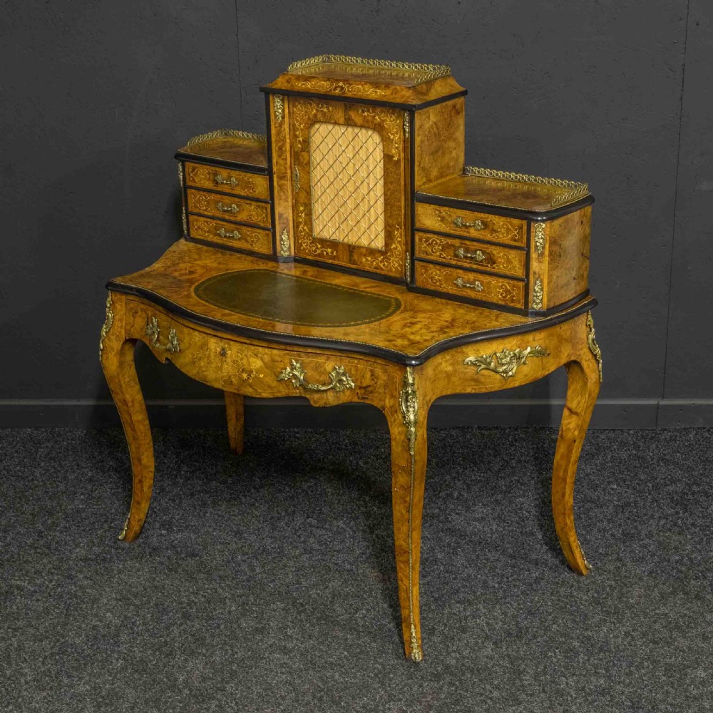 A Victorian burr walnut bonheur de jour featuring floral marquetry inlays, gilt brass mounts, cabriole legs, and a green leather writing surface.