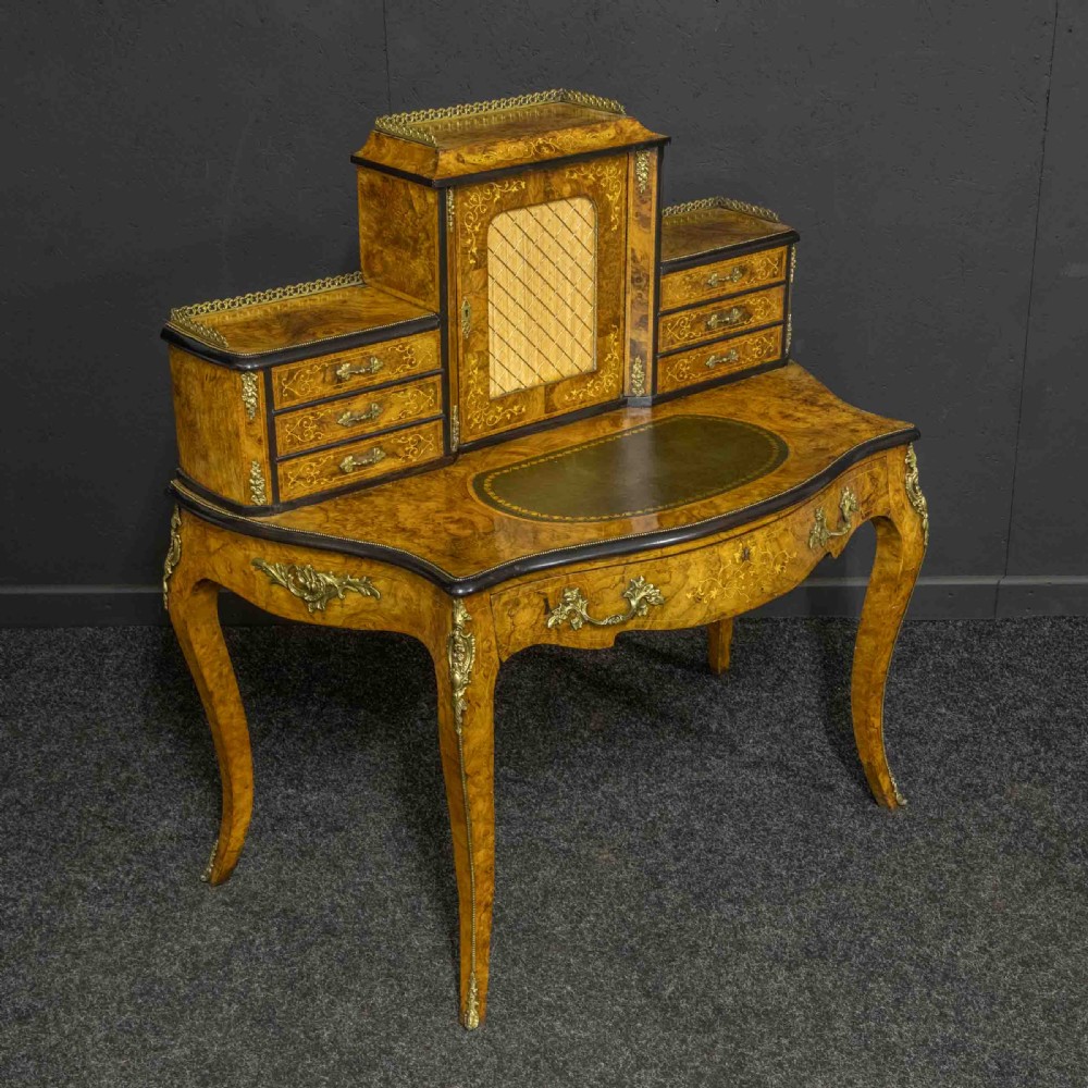 A Victorian burr walnut bonheur de jour featuring floral marquetry inlays, gilt brass mounts, cabriole legs, and a green leather writing surface. View VI