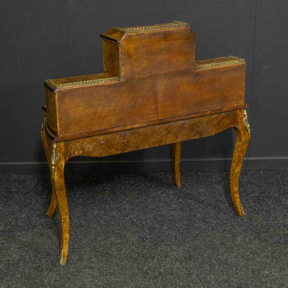 A Victorian burr walnut bonheur de jour featuring floral marquetry inlays, gilt brass mounts, cabriole legs, and a green leather writing surface. View VIII