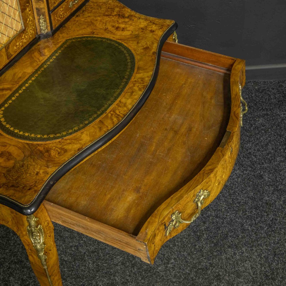 A Victorian burr walnut bonheur de jour featuring floral marquetry inlays, gilt brass mounts, cabriole legs, and a green leather writing surface. View X