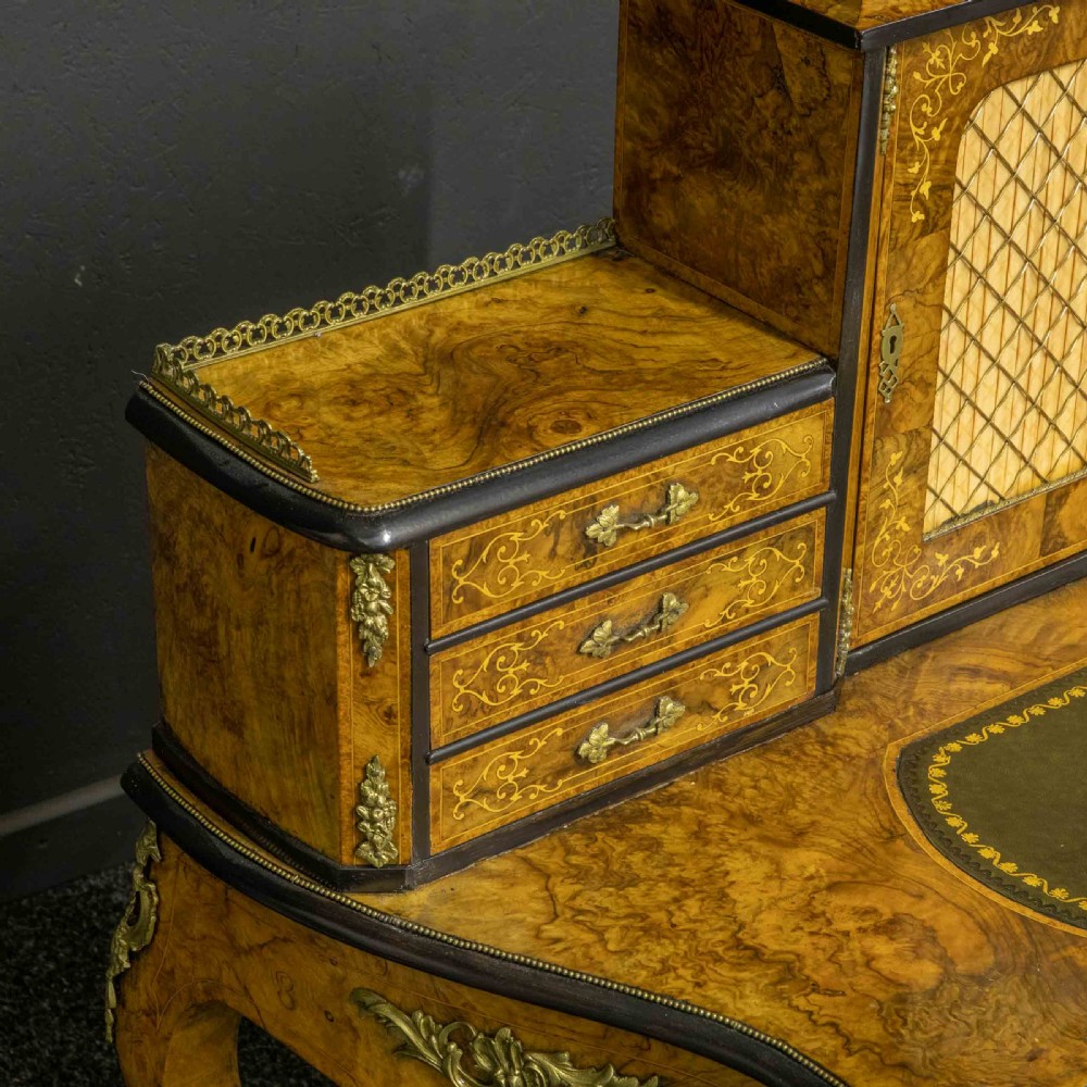 A Victorian burr walnut bonheur de jour featuring floral marquetry inlays, gilt brass mounts, cabriole legs, and a green leather writing surface. View XIV