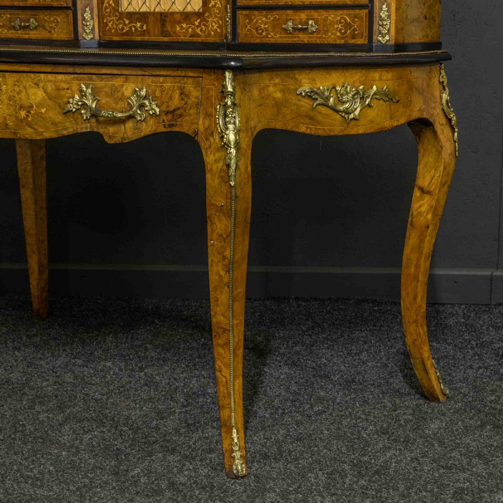 A Victorian burr walnut bonheur de jour featuring floral marquetry inlays, gilt brass mounts, cabriole legs, and a green leather writing surface. View XIX