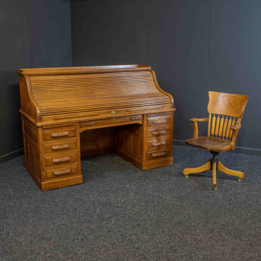 A large Edwardian golden oak roll-top desk featuring a slatted tambour cover, an extensive fitted interior with small drawers and pigeonholes, and twin pedestals with carved wooden handles. View II