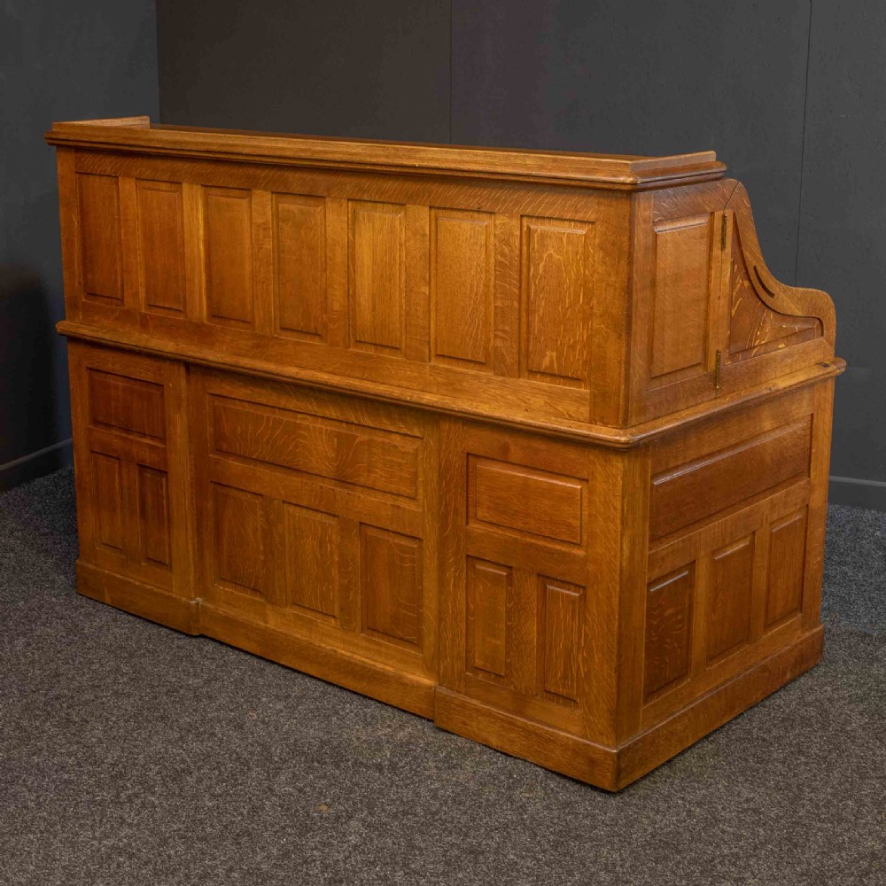 A large Edwardian golden oak roll-top desk featuring a slatted tambour cover, an extensive fitted interior with small drawers and pigeonholes, and twin pedestals with carved wooden handles. View V