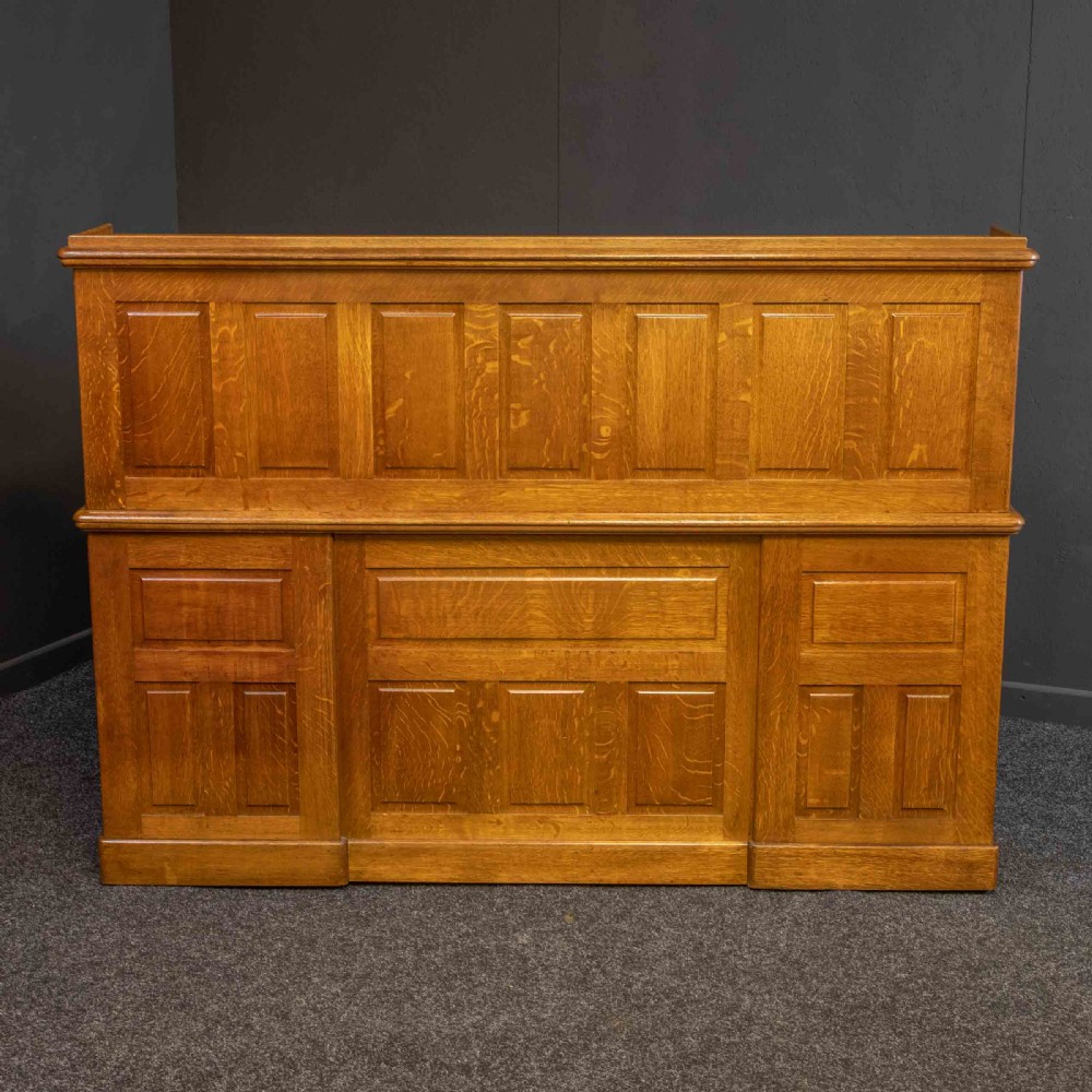 A large Edwardian golden oak roll-top desk featuring a slatted tambour cover, an extensive fitted interior with small drawers and pigeonholes, and twin pedestals with carved wooden handles. View VI