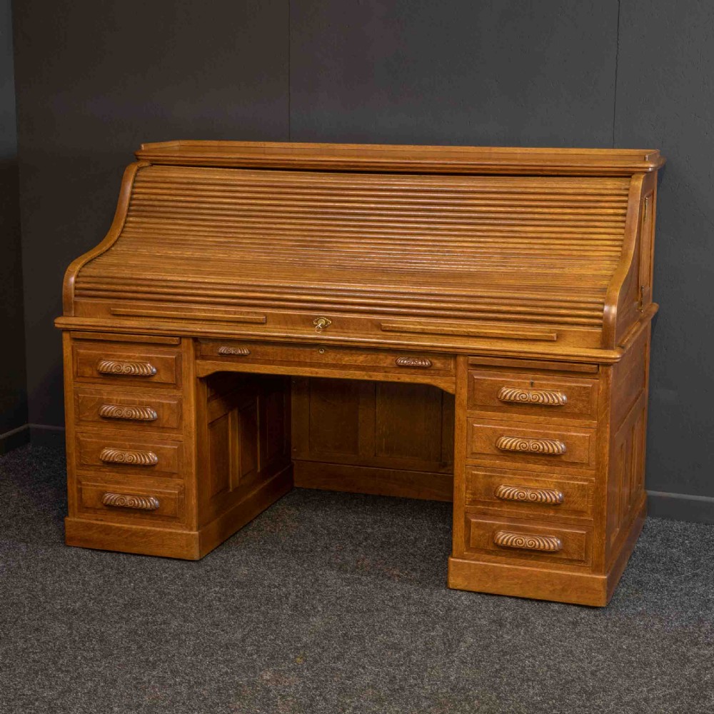A large Edwardian golden oak roll-top desk featuring a slatted tambour cover, an extensive fitted interior with small drawers and pigeonholes, and twin pedestals with carved wooden handles. View IX