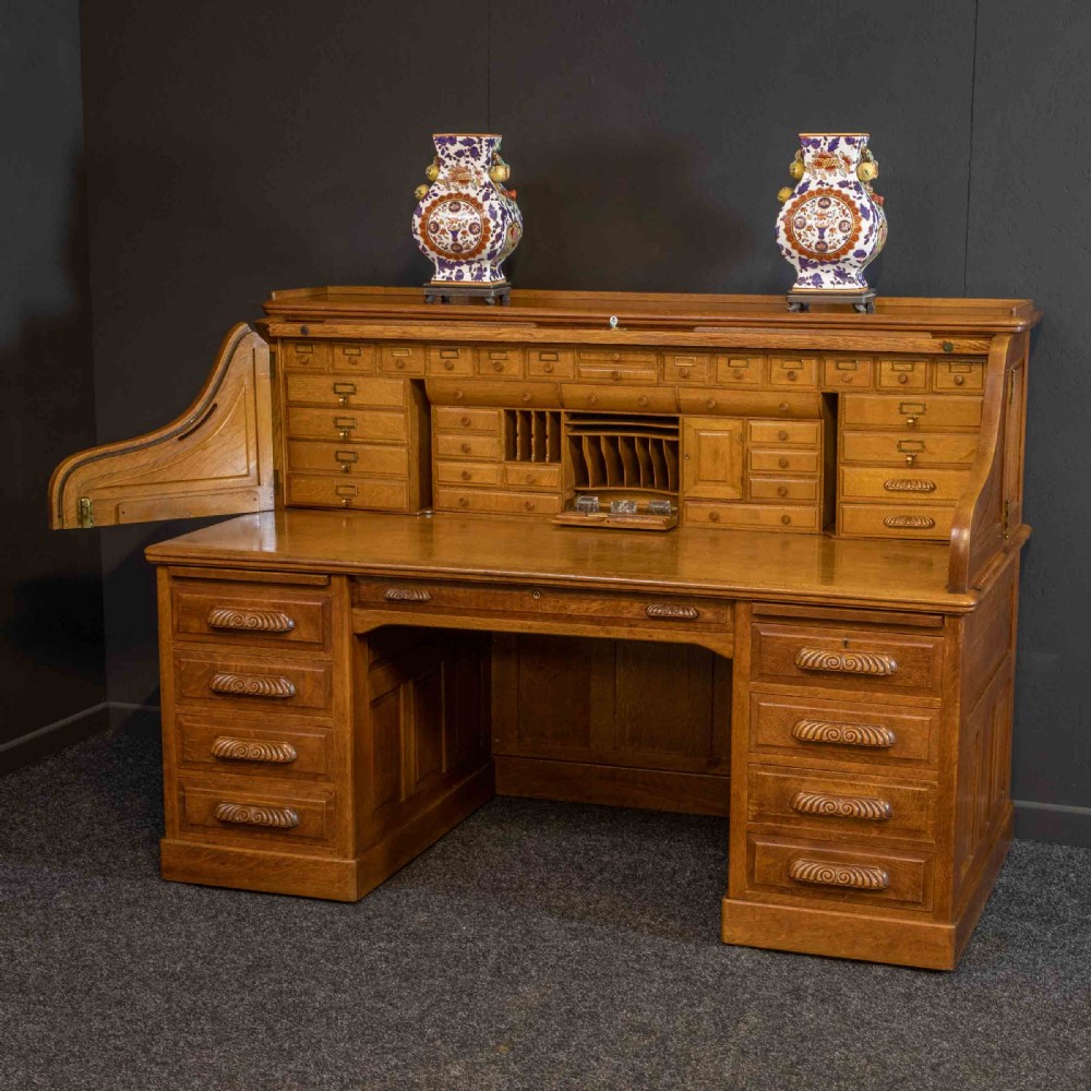 A large Edwardian golden oak roll-top desk featuring a slatted tambour cover, an extensive fitted interior with small drawers and pigeonholes, and twin pedestals with carved wooden handles. View XI